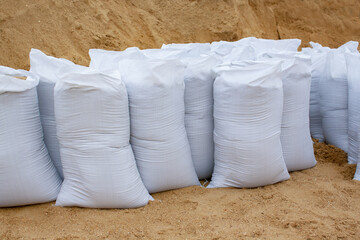 white sandbags stand in a row against a background of sand. building material in the package.