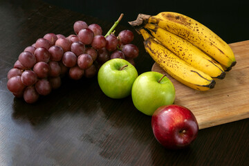 fruit still life with grapes green and red apple and bananas on a black background