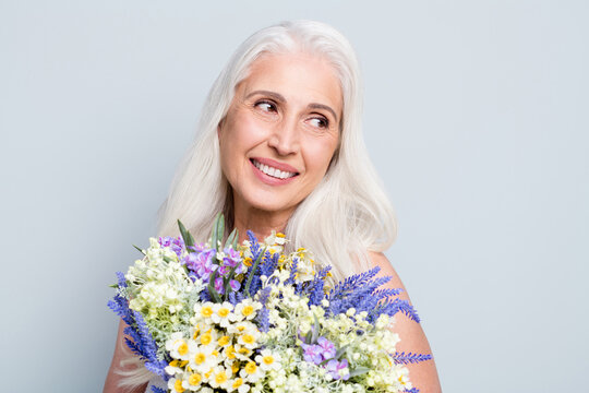 Photo of cute retired woman hold bunch wild flowers look side flirty empty space shy lady isolated grey color background