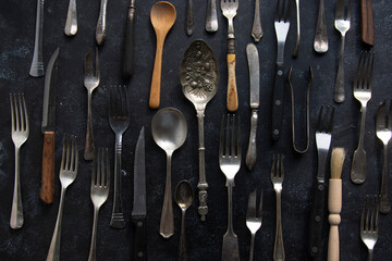 Vintage cutlery, forks, spoons, and knives on dark background, top view. Food photo styling, props.