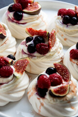Mini Pavlova meringue cakes decorated with berries and figs.