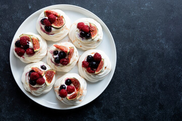 Mini Pavlova meringue cakes decorated with berries and figs.