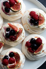 Mini Pavlova meringue cakes decorated with berries and figs.