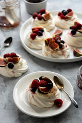 Mini Pavlova meringue cakes decorated with berries and figs.