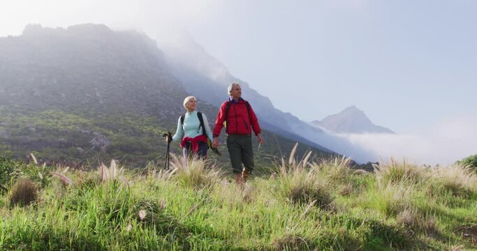 Senior hiker couple with backpacks and hiking poles holding hands and walking while hiking