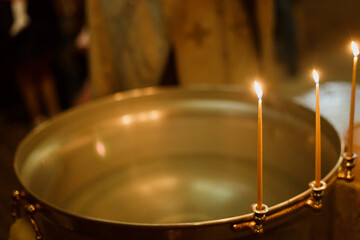 Fototapeta premium The hands of a priest over a basin of water and church candles for the rite of baptism in the Orthodox Church