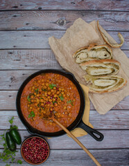 Middle Eastern chickpeas in cast iron pan on wooden table, bread, copy space