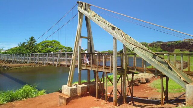 4K right to left 60 fps motion pan of woman walking on the Hanapepe swinging bridge which is a Wooden bridge built in the early 1900's,Kauai,Hawaii,USA