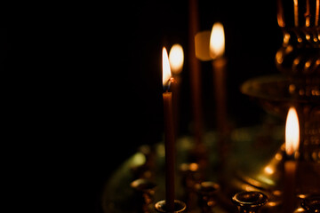 Photo with film grain: Wax candles in a wooden Orthodox church on a golden candlestick in a dark...