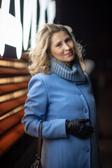 Blonde young beautiful woman in a blue coat posing in the night city.