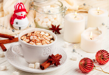 Coffee, cocoa, hot chocolate with marshmallows and cinnamon in a white Cup on a wooden table. New year. The concept of comfort and relaxation with candles, spices and Christmas toys. Selective focus