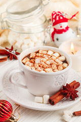 Coffee, cocoa, hot chocolate with marshmallows and cinnamon in a white Cup on a wooden table. New year. The concept of comfort and relaxation with candles, spices and Christmas toys. Selective focus