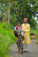 Naklejka premium Young indian farmer and his son going to school on cycle