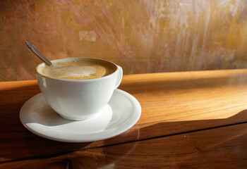 white cup of coffee with a wooden table and yellow late afternoon sun illuminating