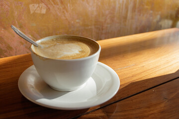 white cup of coffee with a wooden table and yellow late afternoon sun illuminating