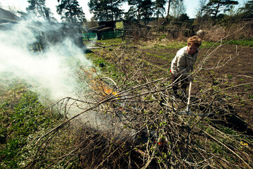 Elderly woman burns branches on her farm.