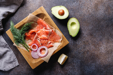 Top view of smoked salmon slices with onion, dill, lemon and avocado on a table with copy space.