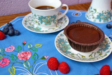 Porcelain set with coffee, a chocolate coulant on a blue floral embroidered tablecloth surrounded by blueberries and raspberries