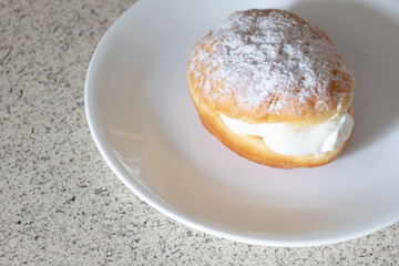 A powdered vanilla cream filled donut on a white plate waiting to be served.