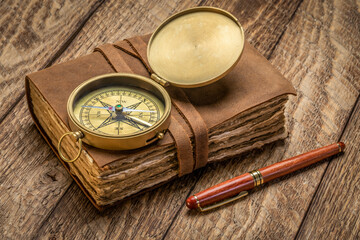 Fototapeta na wymiar retro leather-bound journal with decked edge handmade paper pages, antique brass compass and a stylish pen on a rustic wooden table, journaling concept