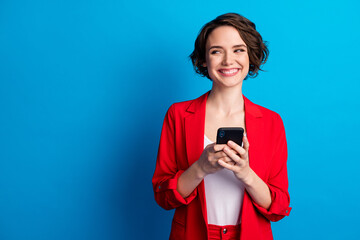 Naklejka premium Portrait of attractive glad cheerful brown-haired lady using gadget looking aside copy space isolated over bright blue color background