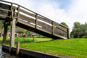 Wooden decorative footbridge over a canal in the Netherlands in the background of plants and buildings.