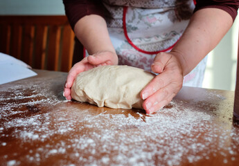 Senior woman hands knead dough on a table in her home kitchen