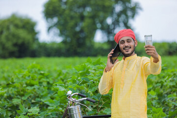Young indian farmer talking on mobile phone and showing money at cotton field