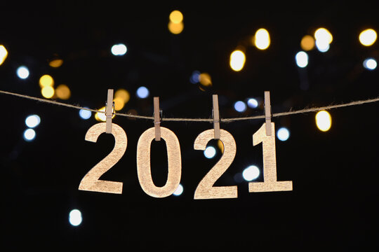Año nuevo de 2021 en letras de madera dorada colgando de una cuerda con luces desenfocadas sobre fondo negro, foto para diseños