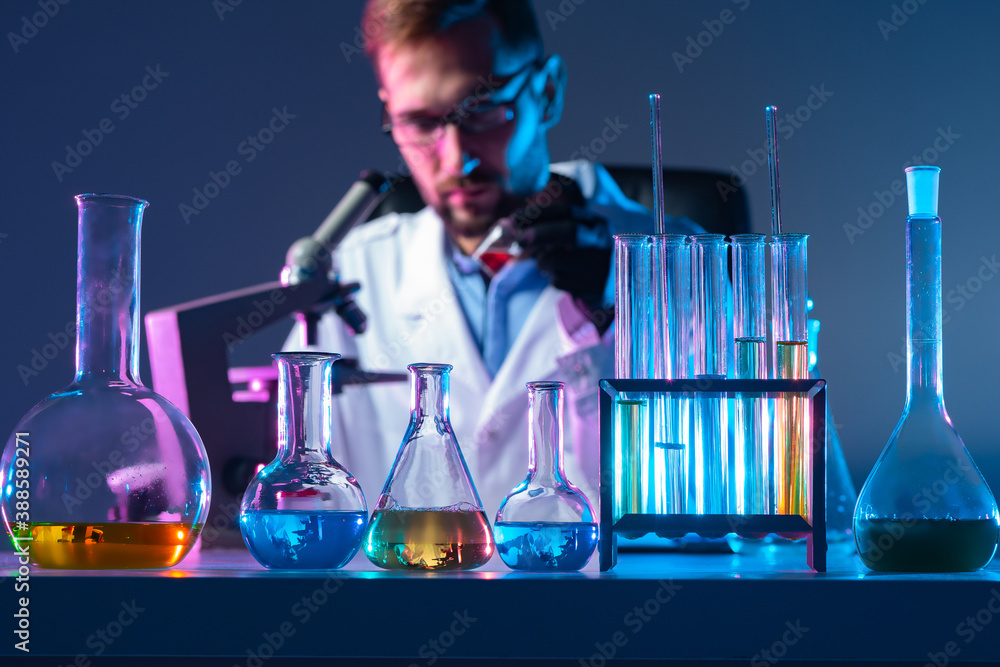 Poster laboratory glassware is on the table. laboratory assistant with a microscope in the background. labo