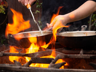 cooking on the grill in a frying pan. frying pan on fire. a man stirs food in a frying pan