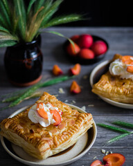 Puff pastry with apricots and whipped cream on a dark background.