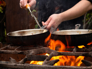 cooking on the grill in a frying pan. frying pan on fire. a man stirs food in a frying pan