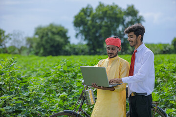 Young indian agronomist showing some information to farmer in laptop at cotton field