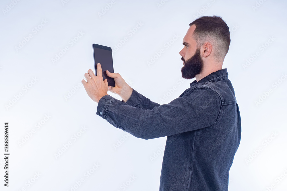 Poster Guy with a beard is using a tablet. Man with an electronic tablet. A man with a gadget on a white background. He is using a gadget with a blank screen. Concept - it uses apps. Tablet apps.