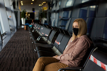 Woman tourist with a mask on her mouth protects against the virus. She sitting with  a distance  and waiting her plane. 
