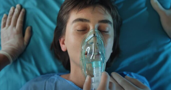 Paramedics putting oxygen inhalation mask and checking pulse on woman face on way to clinic. Close up of millennial woman mumbling while lying on medical stretcher.Concept of illness