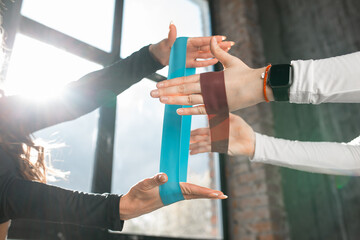 Two girls fitness trainers are doing exercises with training rubber bands in their hands. Close-up of hands with exercise bands