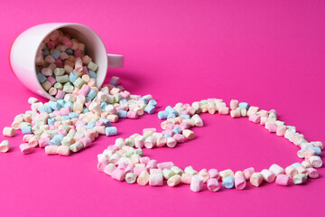 Marshmallow candy in a mug with macaroons on a pink background