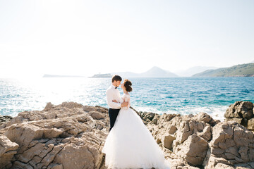 bride and groom are hugging on the rocky beach of the Mamula island against the background of the Arza fortress