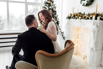 Young couple in love bride and groom posing in studio on background decorated with Christmas tree in their wedding day at Christmas. Enjoy a moment of happiness and love.