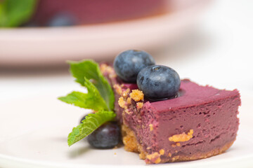 Slice of  baked vanilla and berries flavour cheesecake swirled with blueberry sauce on a digestive biscuit crumb decorated berries and mint