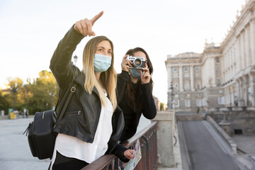 Some travelling girls looking and photographing a part of the city. Both are wearing face masks. Concept of tourism and new normal.