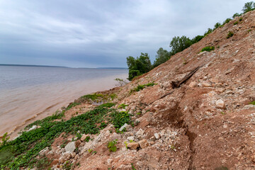 High bank of red clay and muddy water of the Volga river bay on a cloudy day.