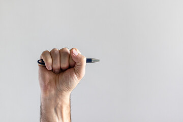Ballpoint pen in male fist on gray background.
