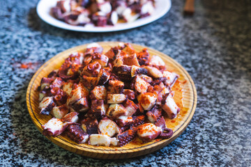 Portion of octopus cut in a wooden plate on a marble background.