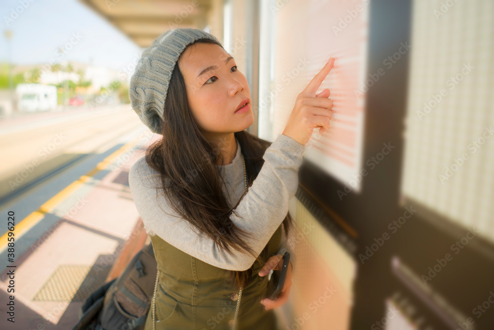 Poster young beautiful and happy Asian Chinese woman waiting the train on station platform bench checking travel and itinerary schedule on information board