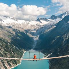 Man in a red tshirtjacket sitting on a suspension bridge above the Alps. Freedom and adventure concept. Touristic activities in Austrian Alps, Europe