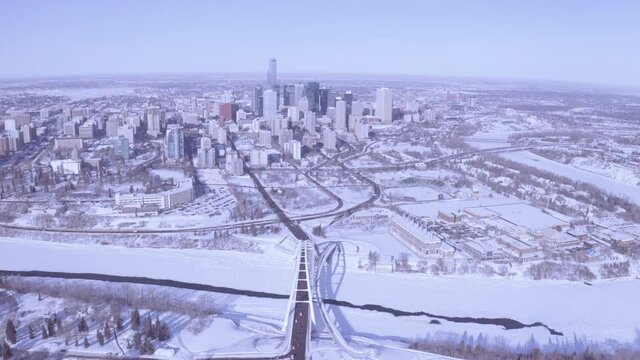 Aerial Rise Over Modern Developing Winter Snow Covered City In Downtown Edmonton Alberta Right Past The Snow Coved North Saskatchewan Rivers With 3 Bridges Connecting.