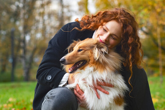 Pretty woman with red hair hugging her collie dog. Female In an autumn park outdoors, cute pet.